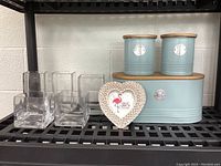 Overview of all items on shelving including bread box, tea and sugar canisters, five glass square vases, and small heart-shaped photo frame