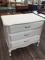 Front view of white painted Baronet dresser showing three drawers with silver handles and decorative carved details.