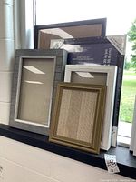 Photo showing assorted shadow boxes and picture frames arranged on a surface near a window.