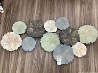 Full view of metal wall art on wood floor showing all circular textured pieces in varied colors and sizes.