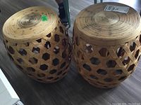 Pair of woven rattan barrel-shaped plant stands with circular solid tops, placed on floor, showing tops and side pattern