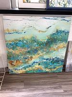 Full image of square canvas print with abstract turquoise and gold design on floor against wall.
