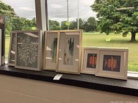Three framed prints arranged on windowsill showing size and artwork variation including two abstract prints and one fish illustration print.