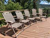 Five folding outdoor chairs lined up on a wooden deck under sunlight, showing the full front and side profiles.