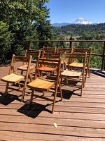 Eight wooden folding chairs arranged on an outdoor wooden deck with scenic mountain view background.