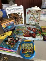 Photo of assorted children's books, board games, crayons and an electronic toy on a table with a soft fabric basket partially visible