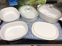 All four white stoneware dishes arranged on cloth with two clear glass Pyrex lids on top, two plastic white lids beside.