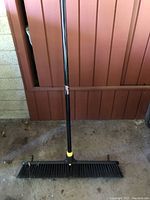 Full view of Quickie floor push broom showing the black handle and wide brush head.
