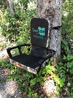 Front angle showing padded backrest with TreeLax logo, seat area with camouflage fabric, mounted on tree with straps attached.