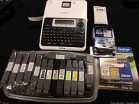 Brother P-touch label maker with keyboard and display surrounded by 16 label cartridges in various colors and widths, some loose others packaged