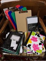 Full display of all paper products and clipboards on a wooden chair, showing various sizes and styles of notebooks and notepads with 4 clipboards behind.