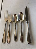 Close-up view of one dinner fork, one salad fork, one teaspoon, one soup spoon, and one dinner knife.