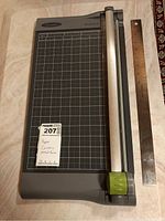 Full view of Swingline SmartCut paper cutter beside the metal ruler on a tiled surface.