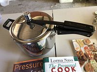 Pressure cooker with lid and handle, showing stainless steel exterior and pressure release valve knob.