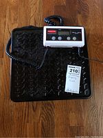 Overall view of Rubbermaid shipping scale with black textured platform and white digital display connected by coiled cord.
