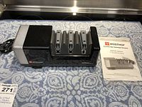 Wusthof electric knife sharpener Model 2933 with 4 sharpening slots and included user manual on a patterned cloth.