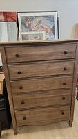 Front view of the Aspenhome wooden chest showing five drawers with dark round knobs, natural wood finish, and slight edge wear.