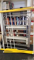 Folded view of the vintage yellow and white clothes drying rack showing metal frame and rods in front of bookshelf.