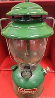 Full front view of vintage green Coleman lantern showing body, glass globe, and vented top.