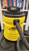 Full view of the Genie wet/dry vacuum showing yellow body, black top with 2.0 HP label, and attached hose.