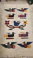 Full view of handwoven beige wool area rug with multicolored bird and floral patterns, laid flat on floor.