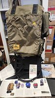 Photo displaying the large olive drab Kelty Super Tioga hiking backpack with external frame and original documentation laid out underneath.
