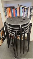 Stack of five small black IKEA stools with round perforated seats and tubular legs, showing the seat tops and legs from front angle.