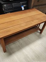 Full view of the rectangular solid wood coffee table with slatted top and lower shelf on a light floor.