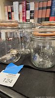 Five vintage Le Parfait French glass canning jars arranged with clamp lids and orange rubber gaskets, shown on black cloth with books in background.