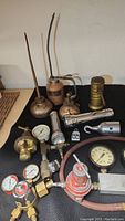 Photo shows a collection of vintage oil cans with flexible spouts, several flashlights in silver and yellow metal finishes, pressure regulators and several pressure gauges with round dials and various fittings.