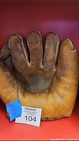 Front view of vintage brown leather baseball glove showing palm, finger stalls, embossed or printed signature/text, black side lacing, with worn and aged leather.