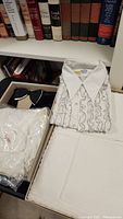 Photo of vintage white men's dress shirt with ruffles and large collar alongside neatly folded white fabric pieces and a black bow tie inside a box.