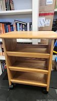 Front view showing the full cart with three open wood shelves and rounded top edge on wheels.