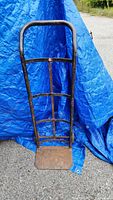 Front view of antique dolley hand truck with metal frame and solid wheels, showing the arched handle and base plate.