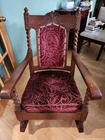 Front view showing detailed red/burgundy fabric upholstery with floral pattern and wooden carved decorative elements.