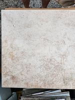 Close-up photo of single ceramic tile showing mottled beige glazed surface with texture.