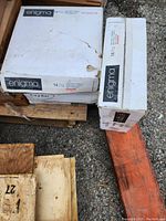 Photo of three unopened cardboard boxes labeled 'Enigma HD Ceramic Tile 14 pcs' stacked on a wooden pallet outdoors.