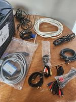 Several different cables and cords spread on table showing HDMI, VGA and RCA cables, audio cables, and various power cords coiled or loose