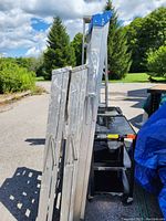Two aluminum ladders folded and standing upright outdoors with visible paint marks and wear on their steps and sides.