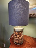 Photo of a table lamp with a glass base filled with corks and a dark blue fabric drum lampshade.