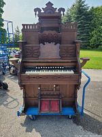 Front view of the antique pump organ showing keyboard, decorative carvings, foot pedals, and music stand.