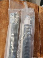 Two Whole Home brand PVC roller blinds, black Saratoga style, packaged in plastic bags showing mounting hardware and roller mechanism.