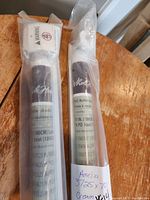 Two rolled-up PVC roller blinds in cream color, packaged in clear plastic with labels showing measurements and style name 'Amelia'.