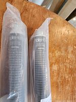 Two dark colored plastic wrapped PVC roller blinds shown from top section on a wooden surface.