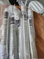 Five Amelia style PVC roller blinds sealed in plastic packaging on a wooden table, showing product labels and rolled fabric texture.