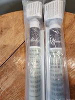 Two black PVC roller blinds in plastic packaging placed on a wooden surface, showing label details including size and brand.