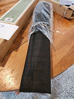 Black fabric Roman shade rolled and sealed in plastic on a wooden table.