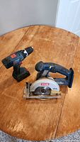 Photo showing Ryobi circular saw and Bosch hand drill on wooden table.