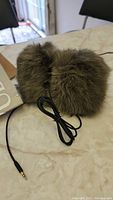 Brown furry smart ear muffs with black wire and 3.5mm headphone jack lying on a surface.