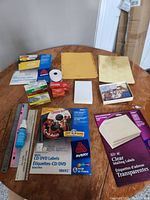 Overview of stationery and label supplies including Avery CD/DVD labels, clear mailing labels, yellow round labels, large yellow envelope, roll of double-sided tape, Velcro dots, small white blank cards, and various loose sheets.